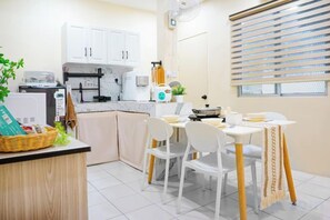 A compact kitchen with white cabinets, a dining table with chairs, and a window with blinds.