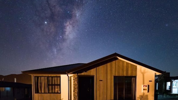 A modern house with a large window and a door, under a starry night sky.