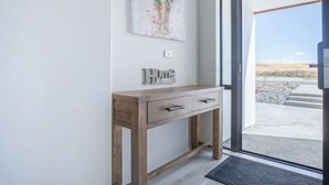 A modern interior with a wooden console table, a colorful abstract artwork, and a view through a glass door.
