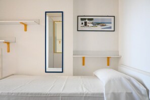 A hotel room with a bed, a mirror, a framed picture, and a small shelf.