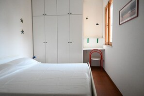 A bedroom with a bed, wardrobe, desk, chair, and a window.