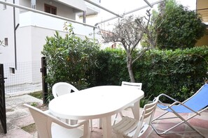 A patio with a white table and chairs, surrounded by greenery and a fence.