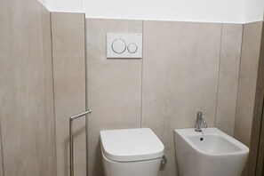 A bathroom with a toilet, bidet, and a wall-mounted control panel.