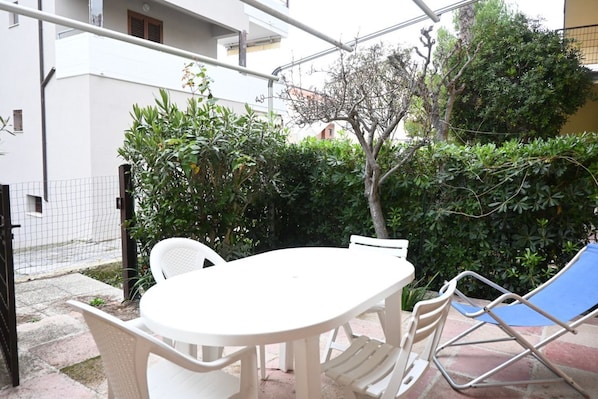 A patio with a white table and chairs, surrounded by greenery and a fence.
