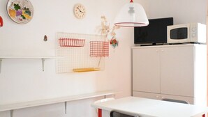 A room with a white table, a red chair, a white cabinet, a black TV, and a white microwave. - M415 – Marcelli, three-room apartment on the ground floor with an external court (Marcelli)