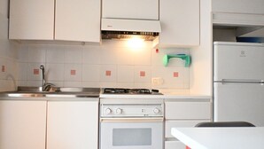 A kitchen with white cabinets, a gas stove, an oven, a sink, and a refrigerator. - M415 – Marcelli, three-room apartment on the ground floor with an external court (Marcelli)