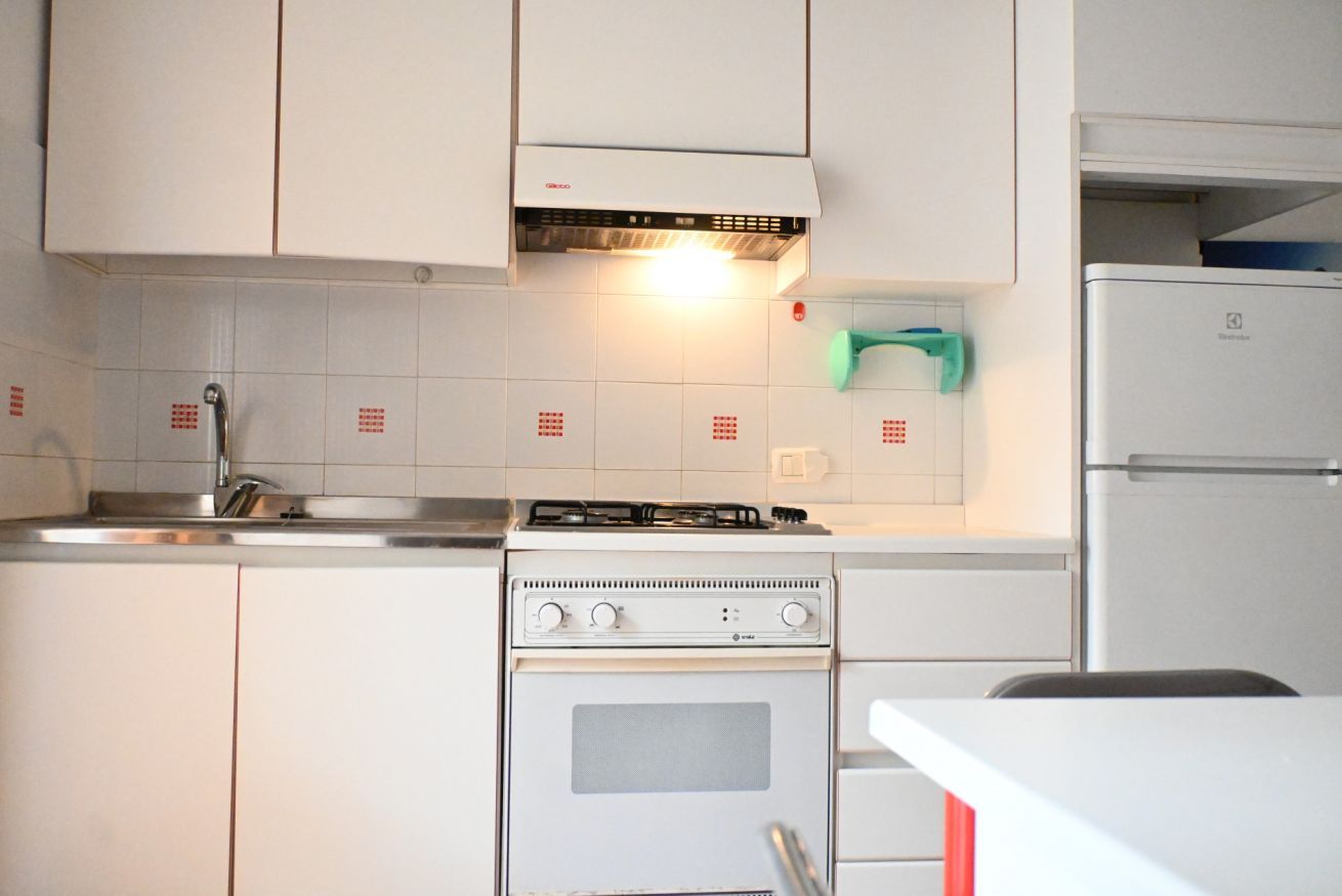 A kitchen with white cabinets, a gas stove, an oven, a sink, and a refrigerator.