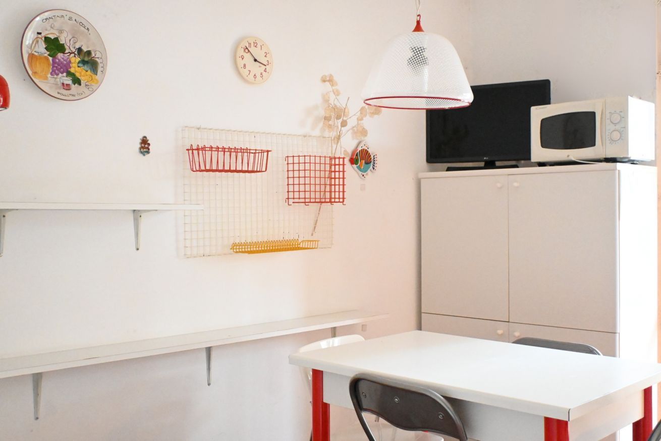 A room with a white table, a red chair, a white cabinet, a black TV, and a white microwave.