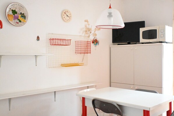 A room with a white table, a red chair, a white cabinet, a black TV, and a white microwave.