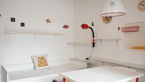A room with a white table, a white bench with a pillow, a red lamp, and wall decorations including fish and a clock. - M415 – Marcelli, three-room apartment on the ground floor with an external court (Marcelli)