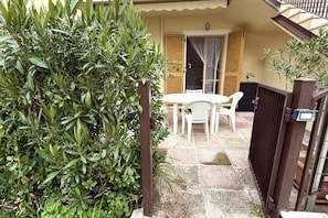 A patio with a table and chairs, a wooden gate, and a hedge.