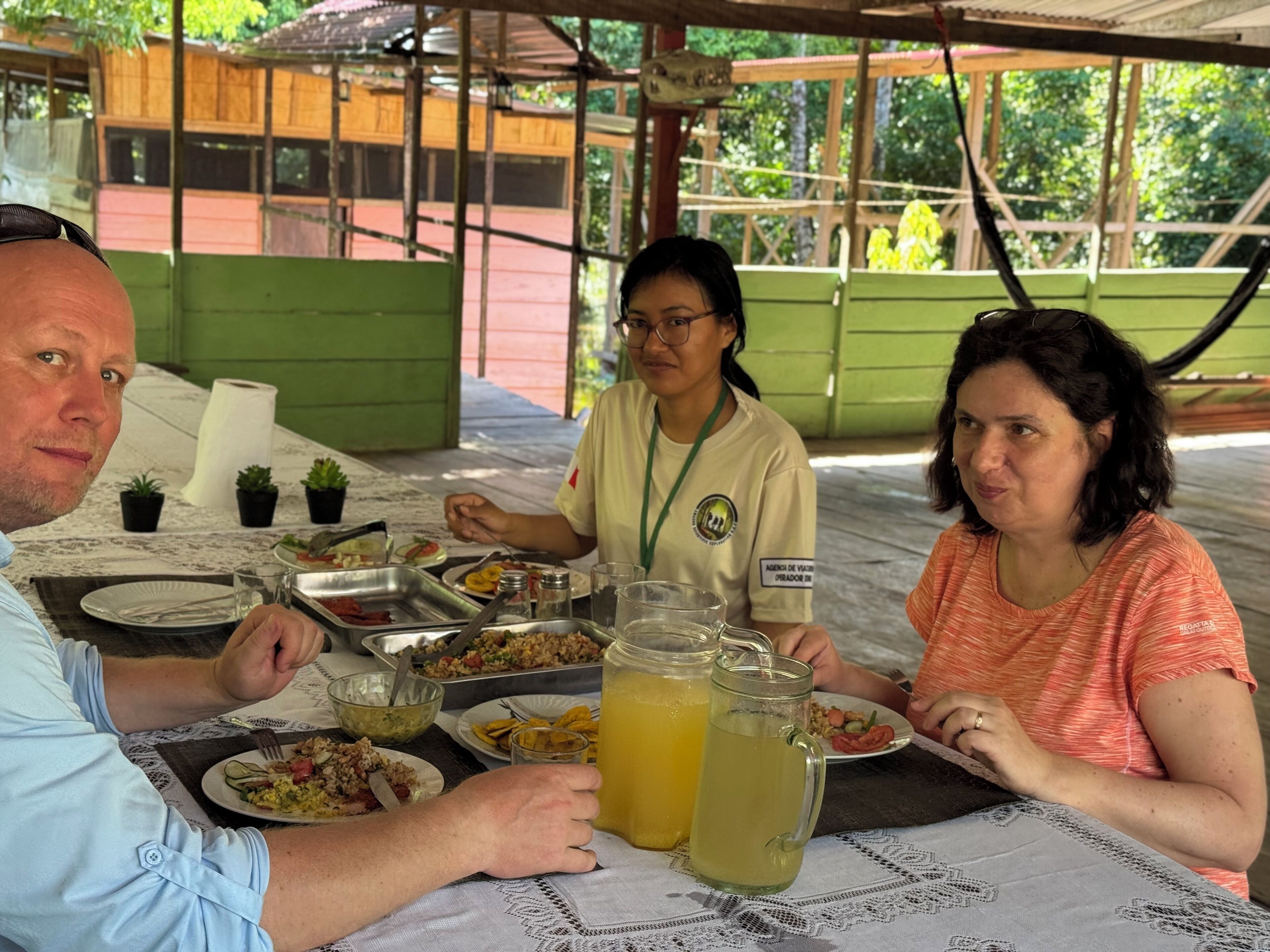 Un groupe de personnes est assis à une table en plein air et déguste différents plats et boissons.
