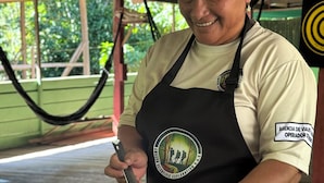 A person serving food at an outdoor dining area with a table set for two, a plate of fried rice, a glass of water, a glass of juice, and a bowl of plantain chips. - ESTACIÓN BIOLÓGICA SMF II ZONA (Indiana)