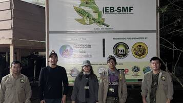 En gruppe mennesker står foran et skilt med logoer og tekst, herunder "EB-SMF" og "Asociación Amazonica".