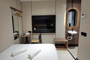 Habitación de hotel con cama, una mesita redonda, una silla, un espejo, televisor y lavabo.