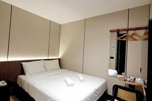 Una habitación de hotel con cama, mesita de noche, silla, espejo y perchero.