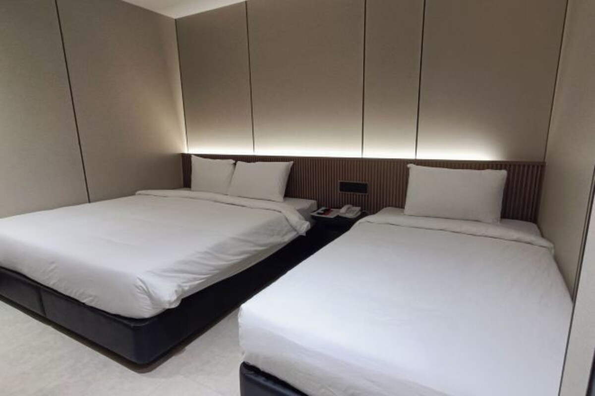 A modern hotel room with two single beds, a dark-colored bench, and a wall-mounted phone.