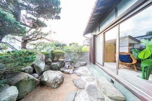Un jardín japonés tradicional con rocas, un pequeño farol de piedra y una silla de madera.
