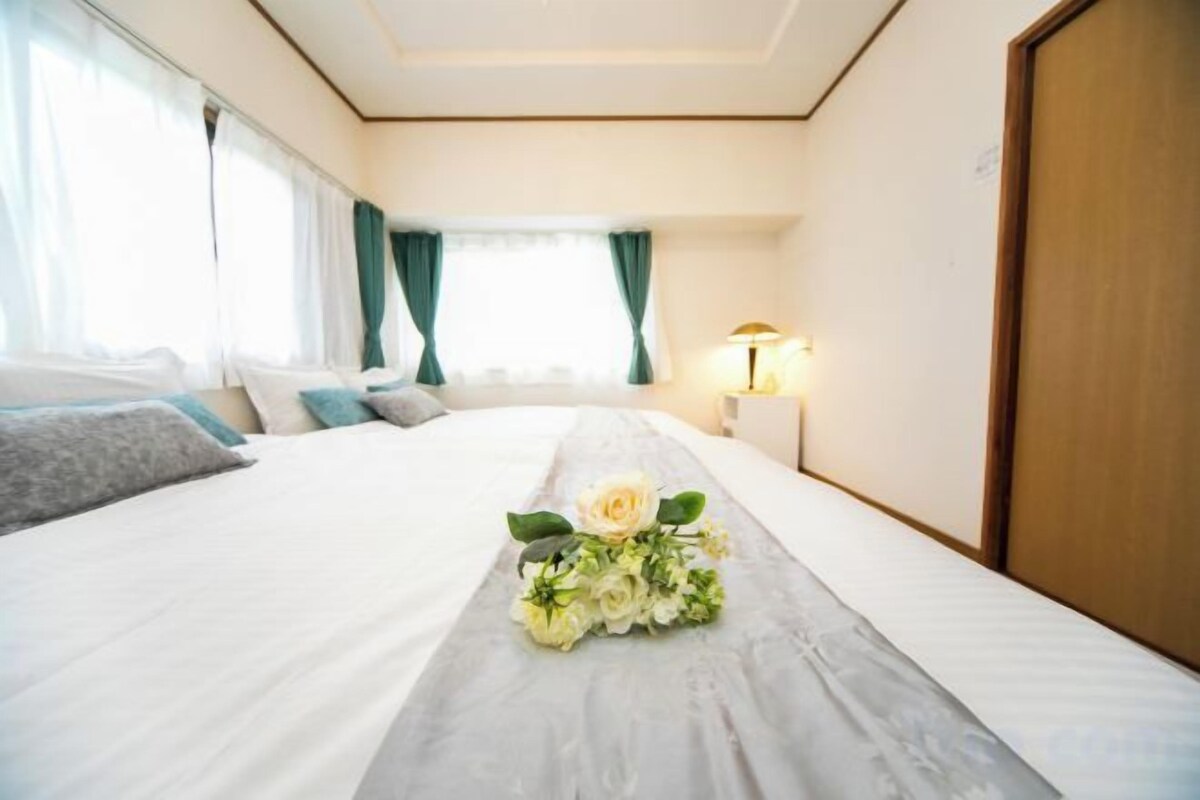 A hotel room with a large bed, a bedside table with a lamp, and a floral arrangement on the bed.