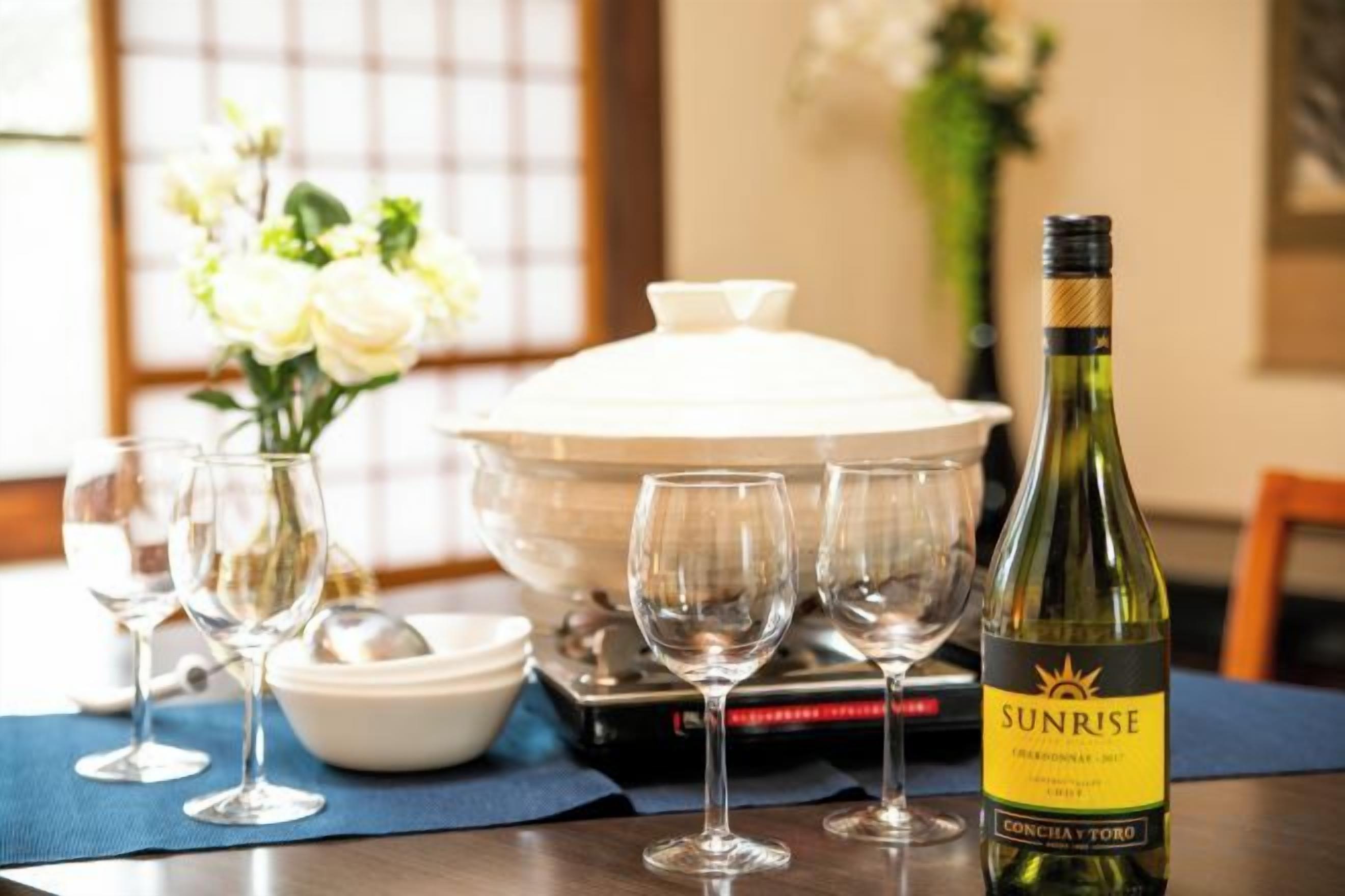 A dining table with a bottle of Sunrise Chardonnay, several wine glasses, a bowl, and a covered dish.
