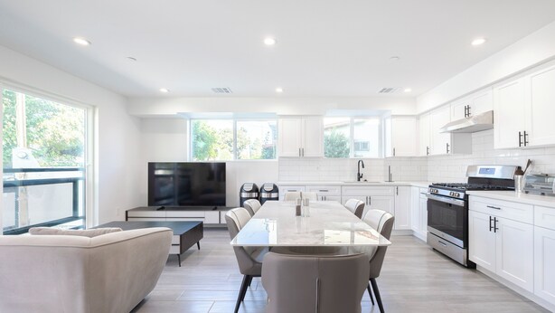 A modern kitchen with white cabinets, a large island, and a dining area with a sofa and chairs. - Spacious 5-bed, 5-bath apartment in charming Los Angeles (Los Angeles)