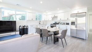 A modern kitchen with white cabinets, a stainless steel refrigerator, a dining table with chairs, a built-in oven, and a large window providing natural light. - Spacious 5-bed, 5-bath apartment in charming Los Angeles (Los Angeles)