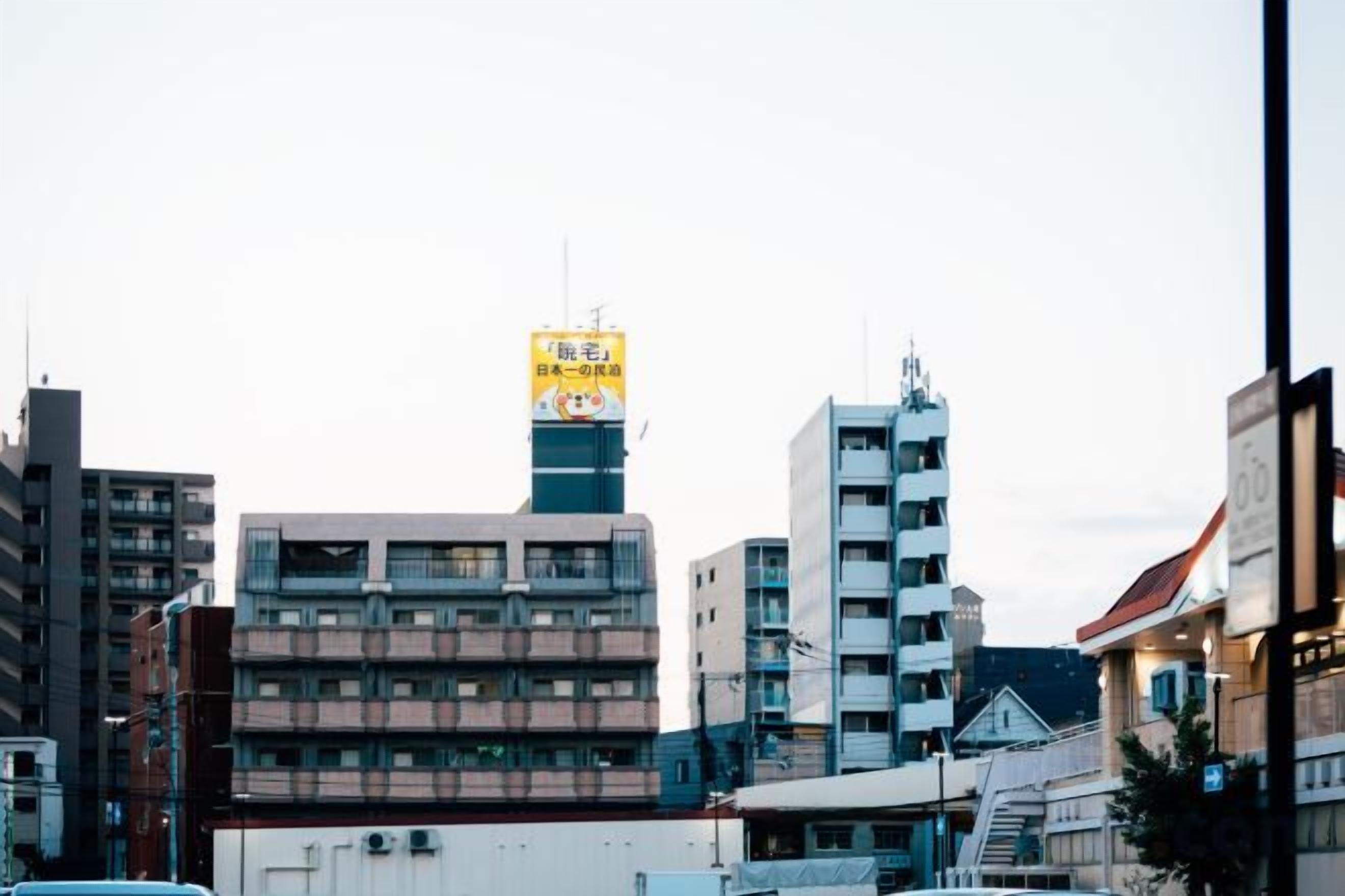 A cityscape with multiple buildings, including a prominent tower with a yellow sign.