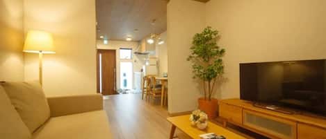 A living room with a sofa, a TV on a wooden stand, a table with a plant, and a lamp.