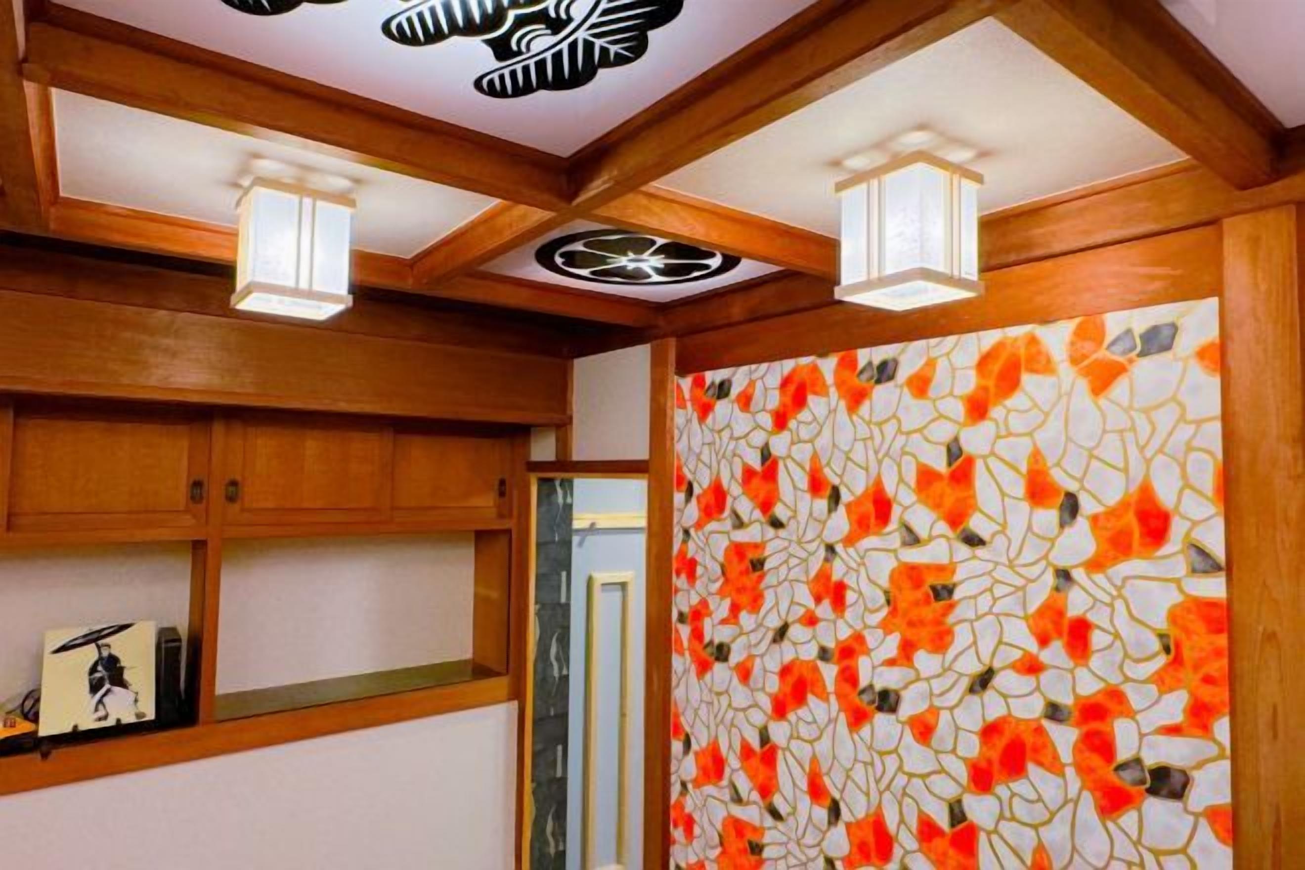 Una habitación con vigas de madera en el techo, un muro con azulejos de estampado floral y una estantería con libros y un cuadro enmarcado.