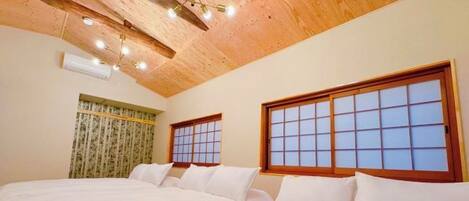 A hotel room with two beds, wooden ceiling beams, a traditional-style window, and a ceiling light fixture.