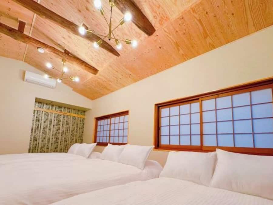 A hotel room with two beds, wooden ceiling beams, a traditional-style window, and a ceiling light fixture.