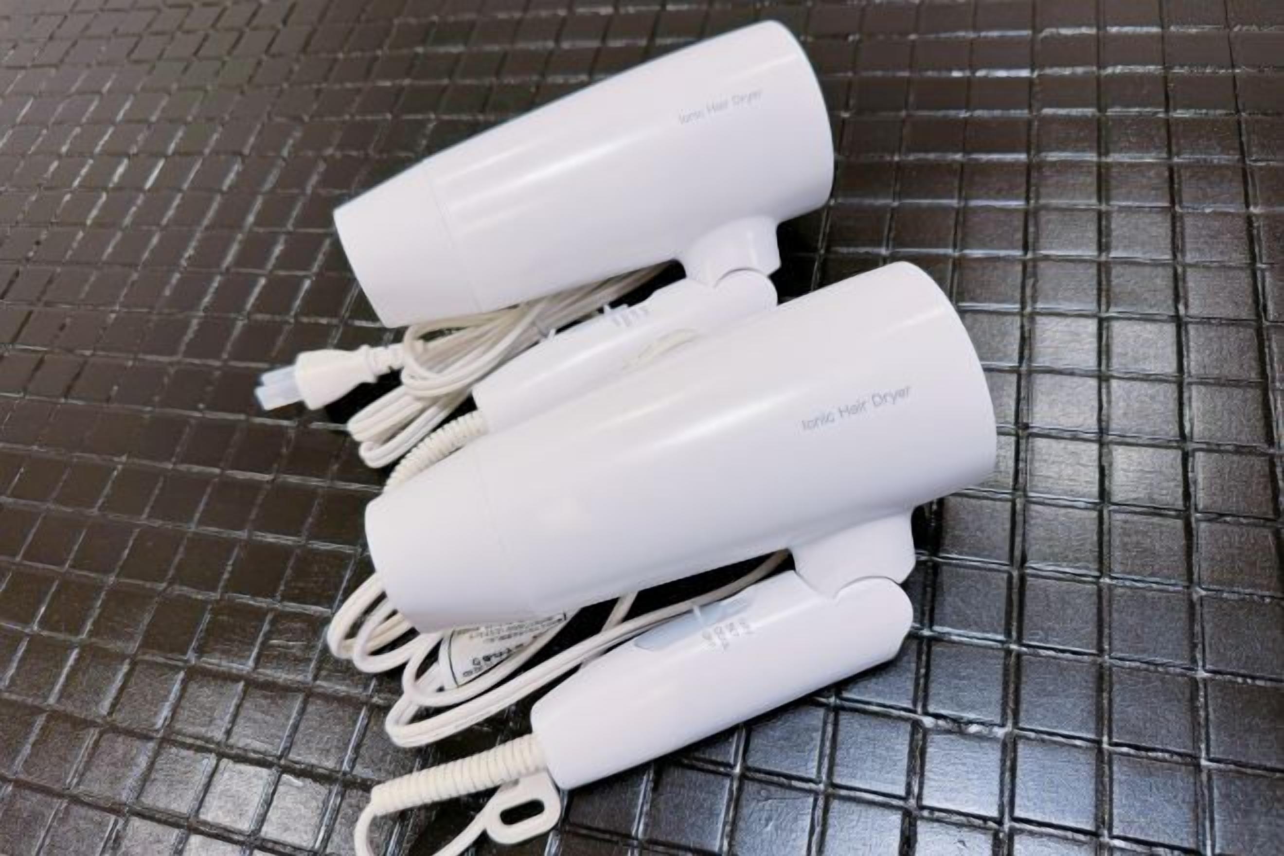 Three white electronic devices with cords, possibly hair dryers, on a tiled surface.