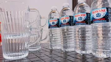 A row of clear glass mugs and four bottles of Roxane water on a shelf.