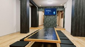 A room with a wooden floor, a central raised platform, and black mats arranged around it. - WholeHouse　Himeji (Himeji)