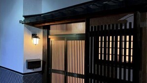 A traditional Japanese gate with vertical slats and a lit lantern on the wall. - WholeHouse　Himeji (Himeji)