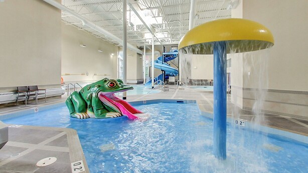 Ein großer Indoor-Wasserpark mit einer großen Froschskulptur, einer Wasserrutsche und einem Poolbereich.