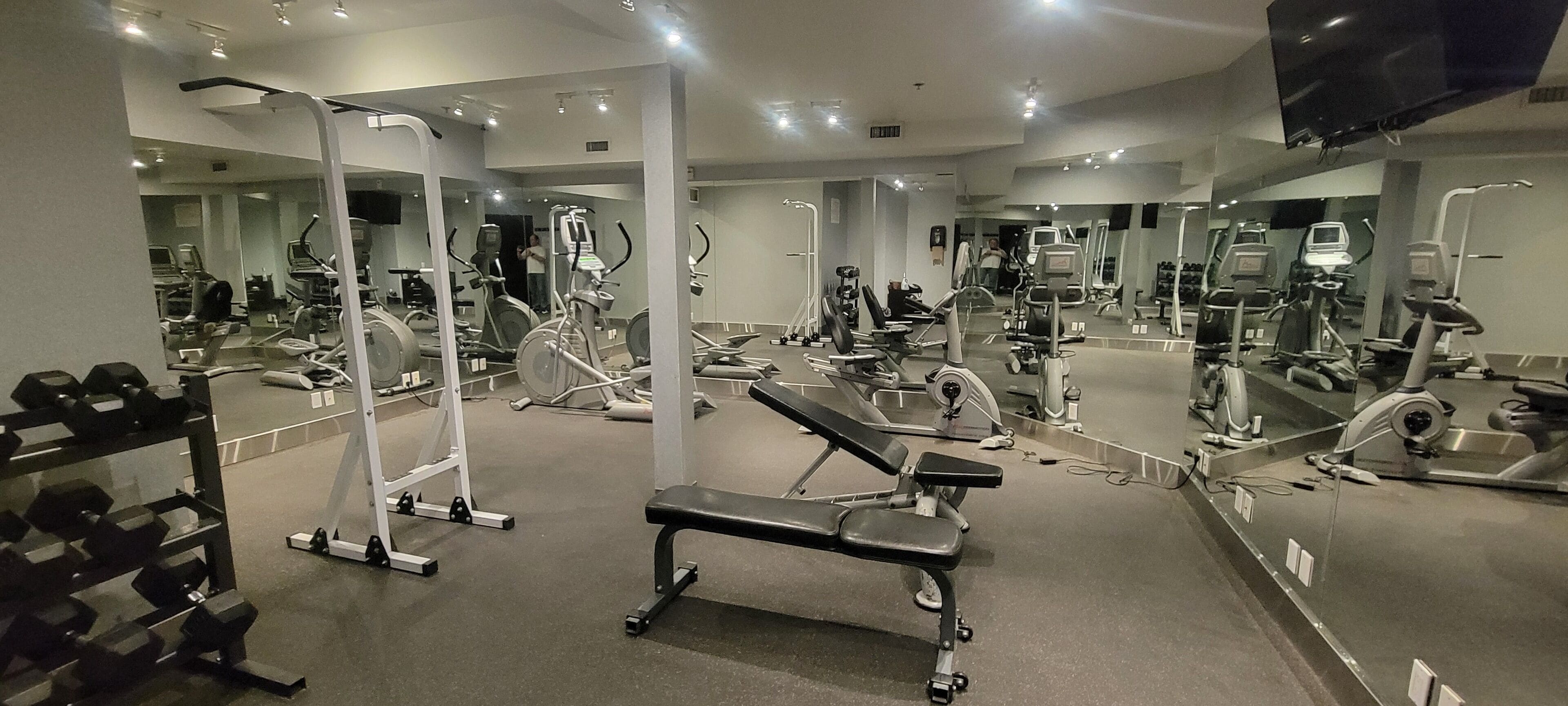 Ein Fitnessstudio mit unterschiedlichen Trainingsgeräten, Spiegeln und einer Bank.
