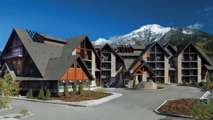 Eine Lodge mit modernem architektonischen Design, mehreren Ebenen und großen Fenstern, vor einer Kulisse schneebedeckter Berge.