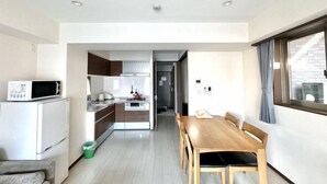 A compact kitchen with a microwave, refrigerator, and dining area with a table and chairs. - Jin Yue guesthouse (Osaka)