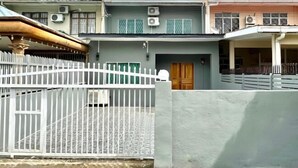 Um edifício residencial de dois andares com um portão branco, aparelhos de ar condicionado e varanda coberta.
