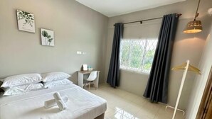 Quarto de hotel com cama, escrivaninha, cadeira, janela com cortinas e luminária pendente.
