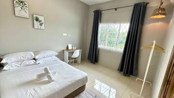 A hotel room with a bed, a desk, a chair, a window with curtains, and a hanging light fixture.