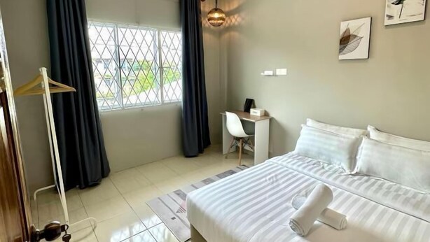 Quarto de hotel com cama, escrivaninha, cadeira, guarda-roupa e janela com cortinas.