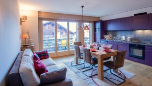 A modern kitchen with purple cabinets, a dining area with a wooden table and chairs, and a sofa with red and black pillows. - Villars Soleil B 13/14 by Interhome (Villars)