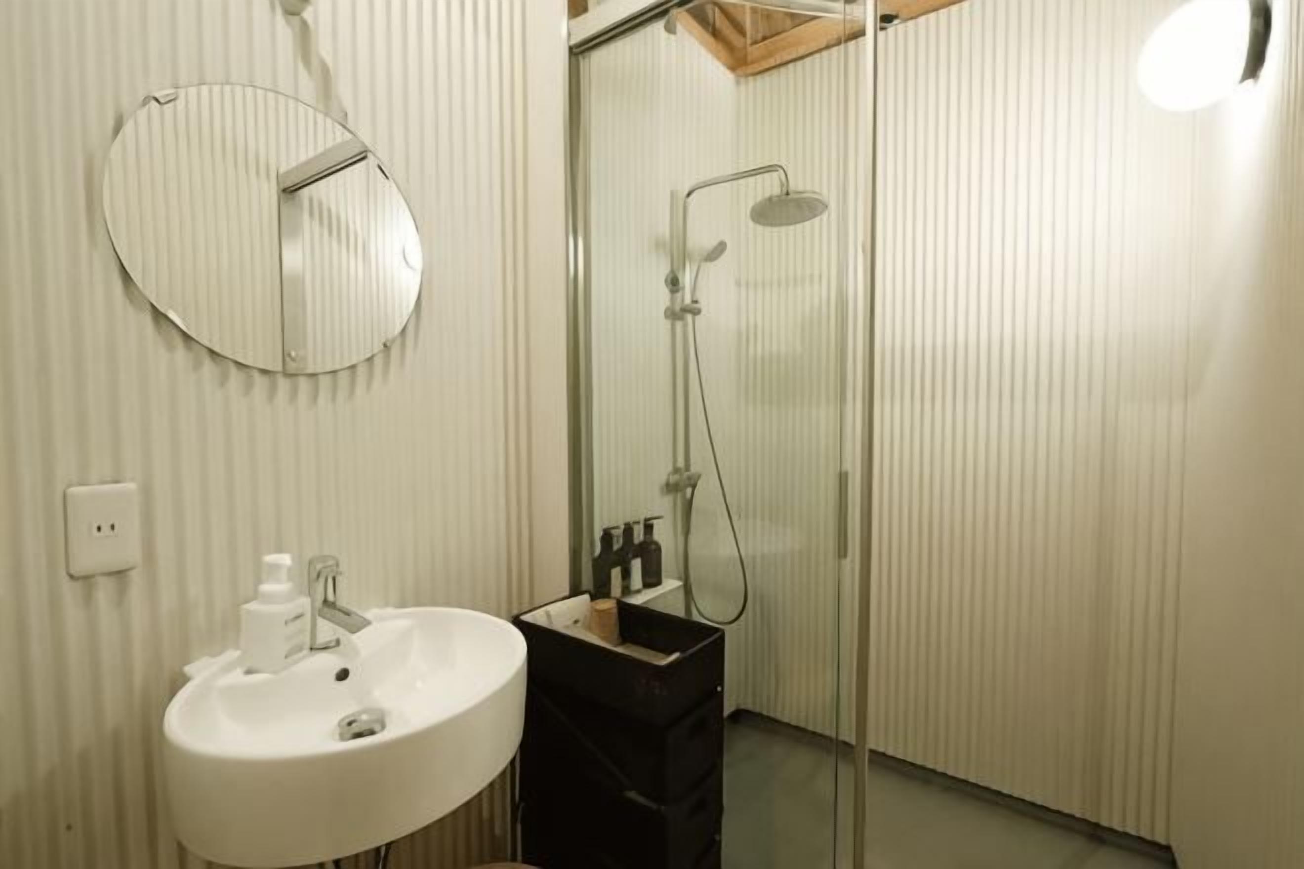 Un baño con un espejo redondo, un lavamanos y una ducha.