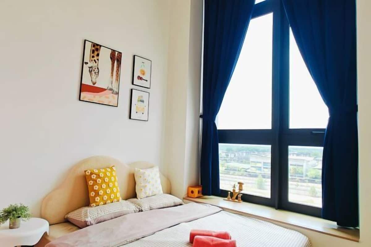 A bedroom with a bed, pillows, a nightstand, a window with curtains, and wall art.