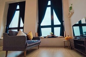 A living room with a sofa, a small table with a plant, and a TV stand. - Chill Lah Homestay (Iskandar Puteri)