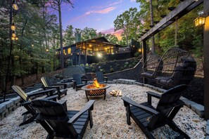 Un espacio exterior acogedor con sillas Adirondack, un brasero y una terraza de madera que conduce a una casa.