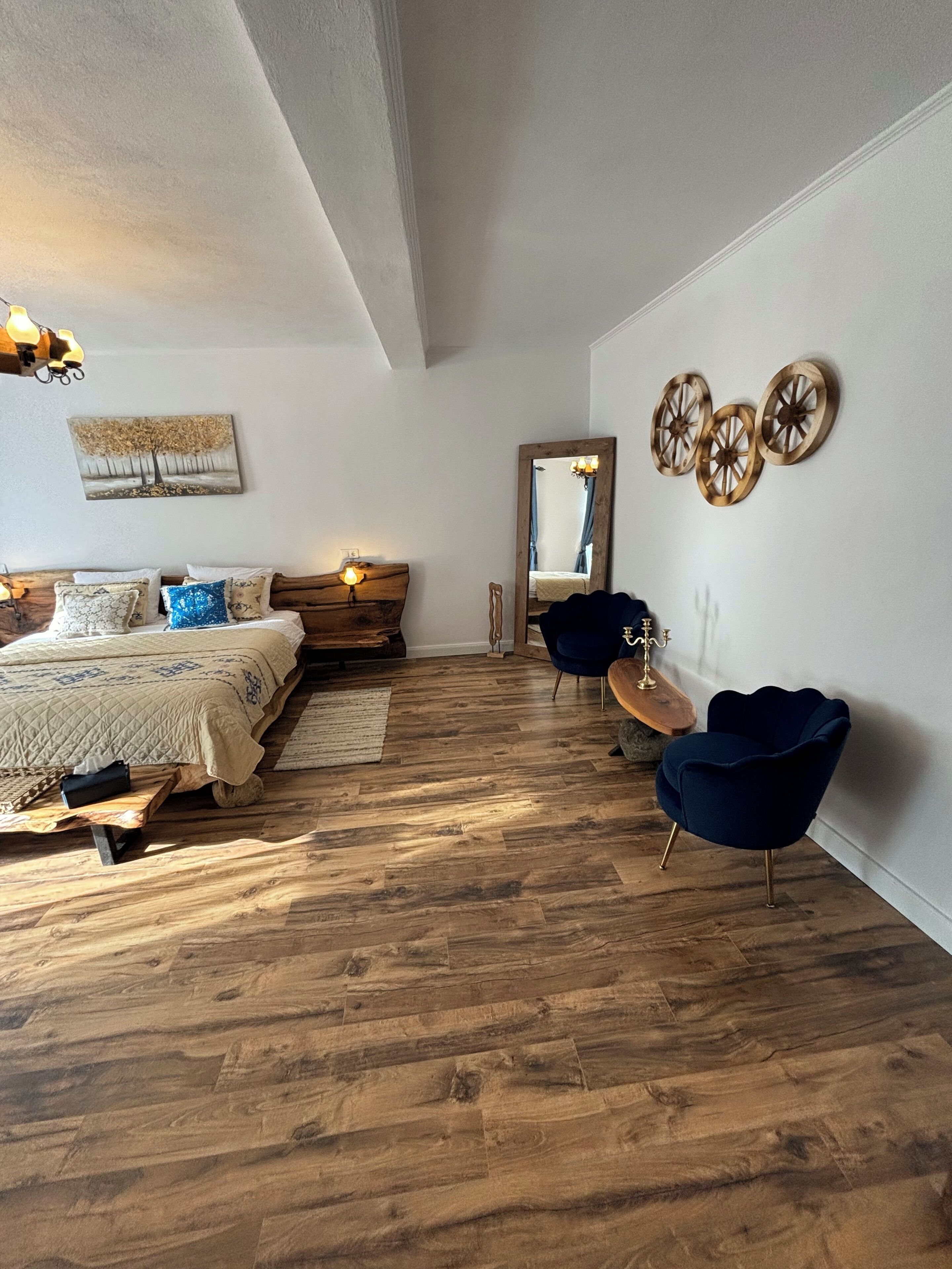 A bedroom with a wooden floor, a bed with a headboard, a dresser, a mirror, and decorative wall art.