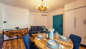 Een eetruimte met een ronde houten tafel gedekt voor vier personen, blauwe gestoffeerde stoelen, een kroonluchter en een blauwe deur op de achtergrond.
